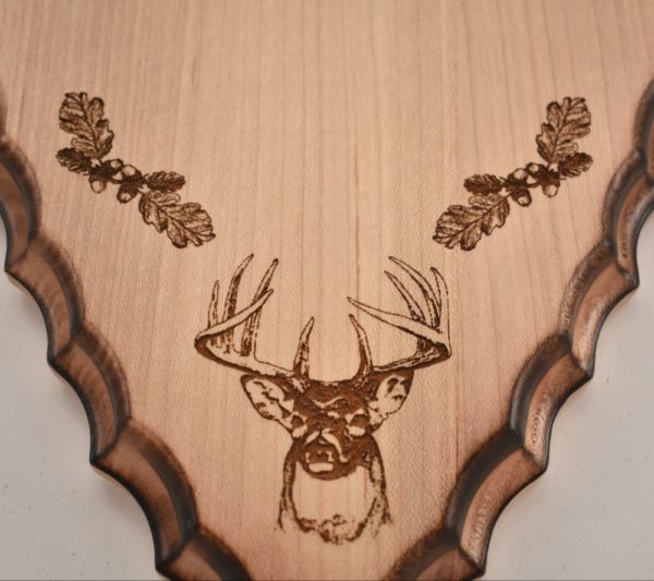 Engraving of the head of a buck and two sprigs of oak on an arrowhead shaped plaque.