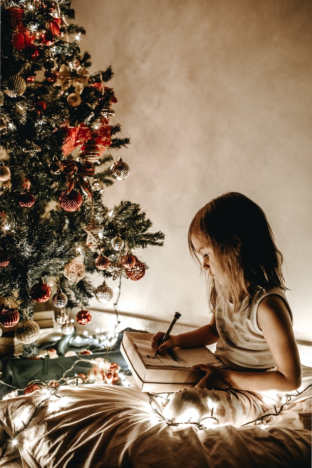 Little girl writing under Christmas tree