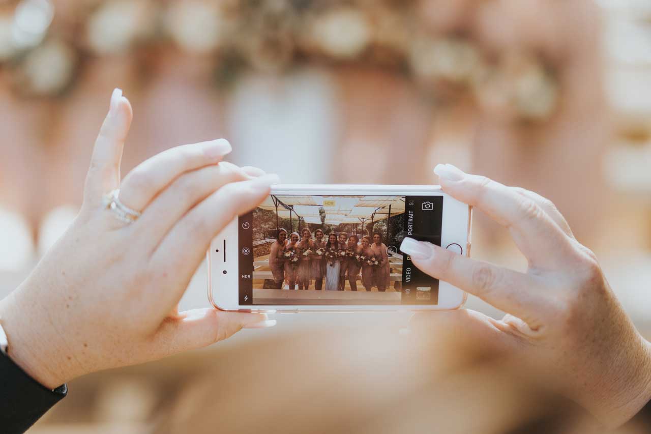 hands taking picture of bridal party on phone